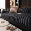 A dark gray thickened plush sofa seat cushion with a beige throw pillow and fluffy accents on a black sofa.