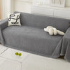 A gray waterproof chenille sofa cover draped over a sofa, with a white decorative pillow and a white rolled object nearby.
