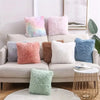 A collection of fluffy velvet throw pillows in pastel shades including pink, purple, blue, and white arranged on a light-colo