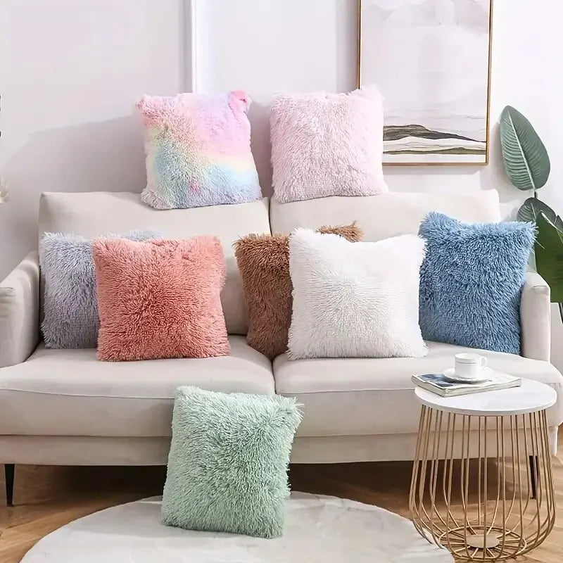 A collection of fluffy velvet throw pillows in pastel shades including pink, purple, blue, and white arranged on a light-colo