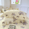 Two floral cotton pillow covers in pale yellow and purple are stacked on a quilted bed with a book.