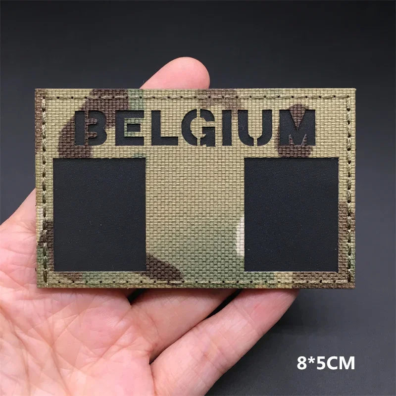 A close-up of a rectangular tactical patch featuring the word BELGIUM in large letters on a camouflage background.