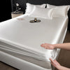 A hand is adjusting a white satin fitted sheet on a mattress, showing the smooth fabric texture.