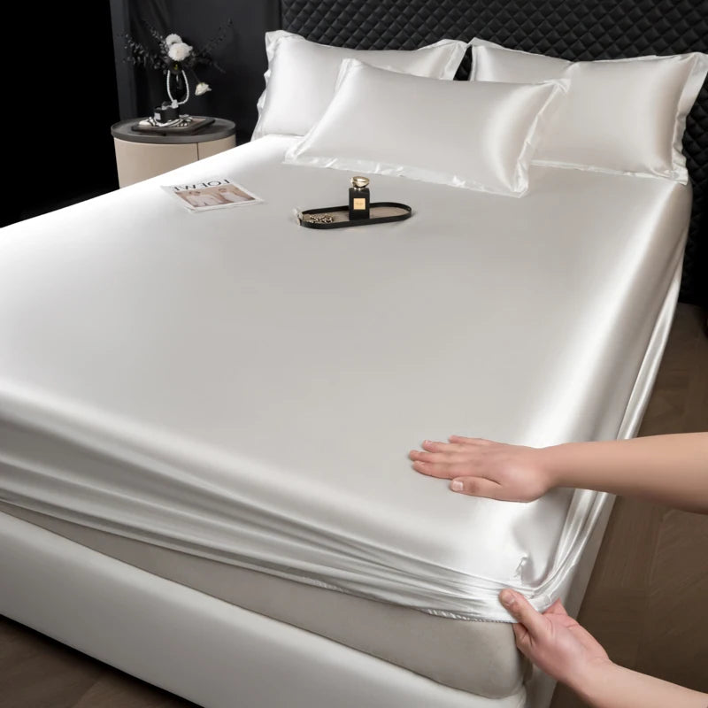 A hand is adjusting a white satin fitted sheet on a mattress, showing the smooth fabric texture.