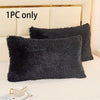 A black faux fur pillow cover is displayed on a white bed, with another matching pillow visible.