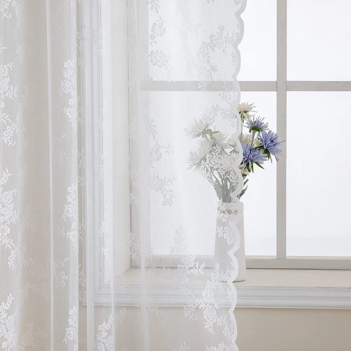 White floral lace sheer curtain hanging in a window with white flowers