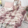A plush rabbit fur throw blanket in shades of pink and mauve draped over a person on a bed.