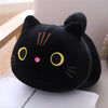 A black soft cat plush pillow cushion with yellow eyes and pink nose resting on a white surface.