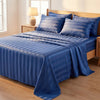 A blue striped satin bedding set with matching pillows on a bed in a bright room.