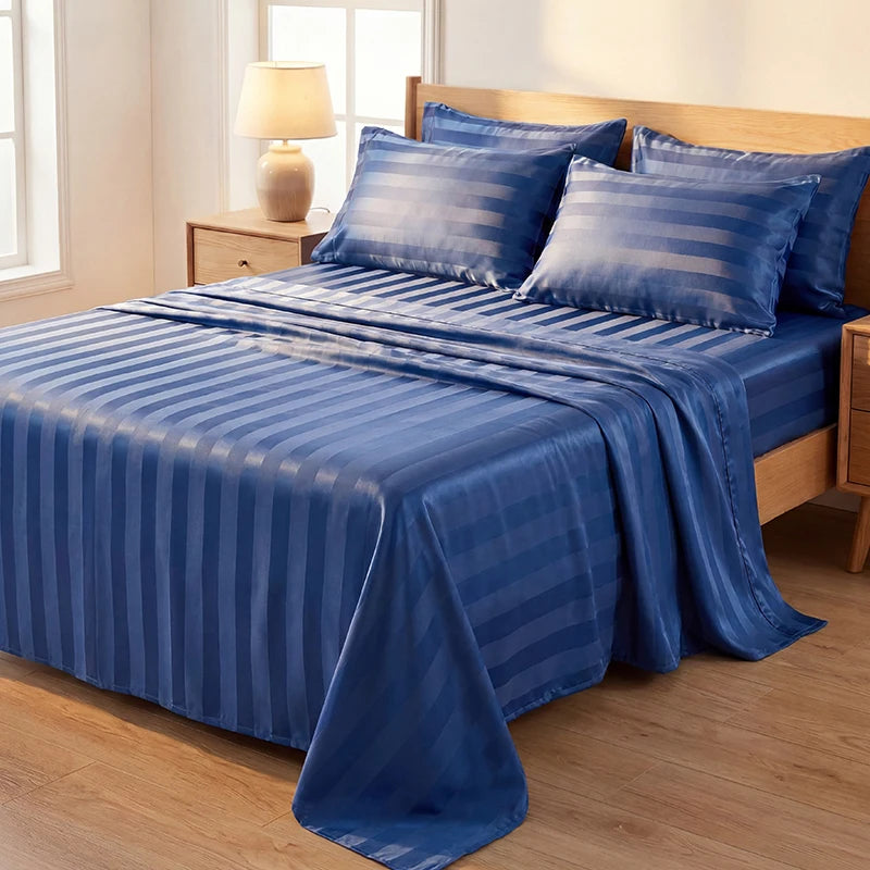 A blue striped satin bedding set with matching pillows on a bed in a bright room.