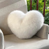 A fluffy white heart-shaped fox fur throw pillow resting on a light gray upholstered chair.