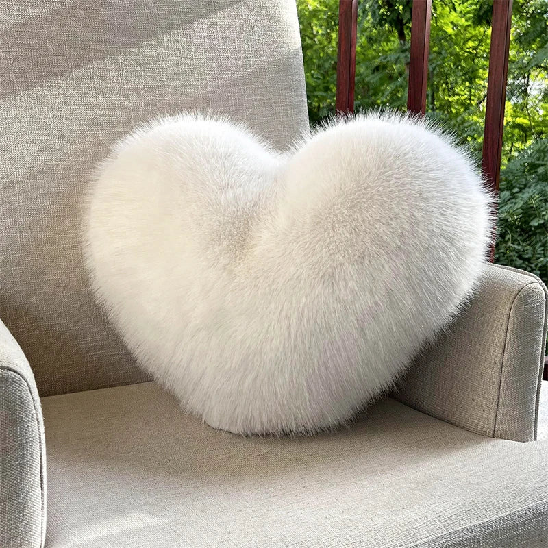 A fluffy white heart-shaped fox fur throw pillow resting on a light gray upholstered chair.