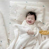A baby is wrapped in a soft white coral fleece flannel blanket with a light pattern.
