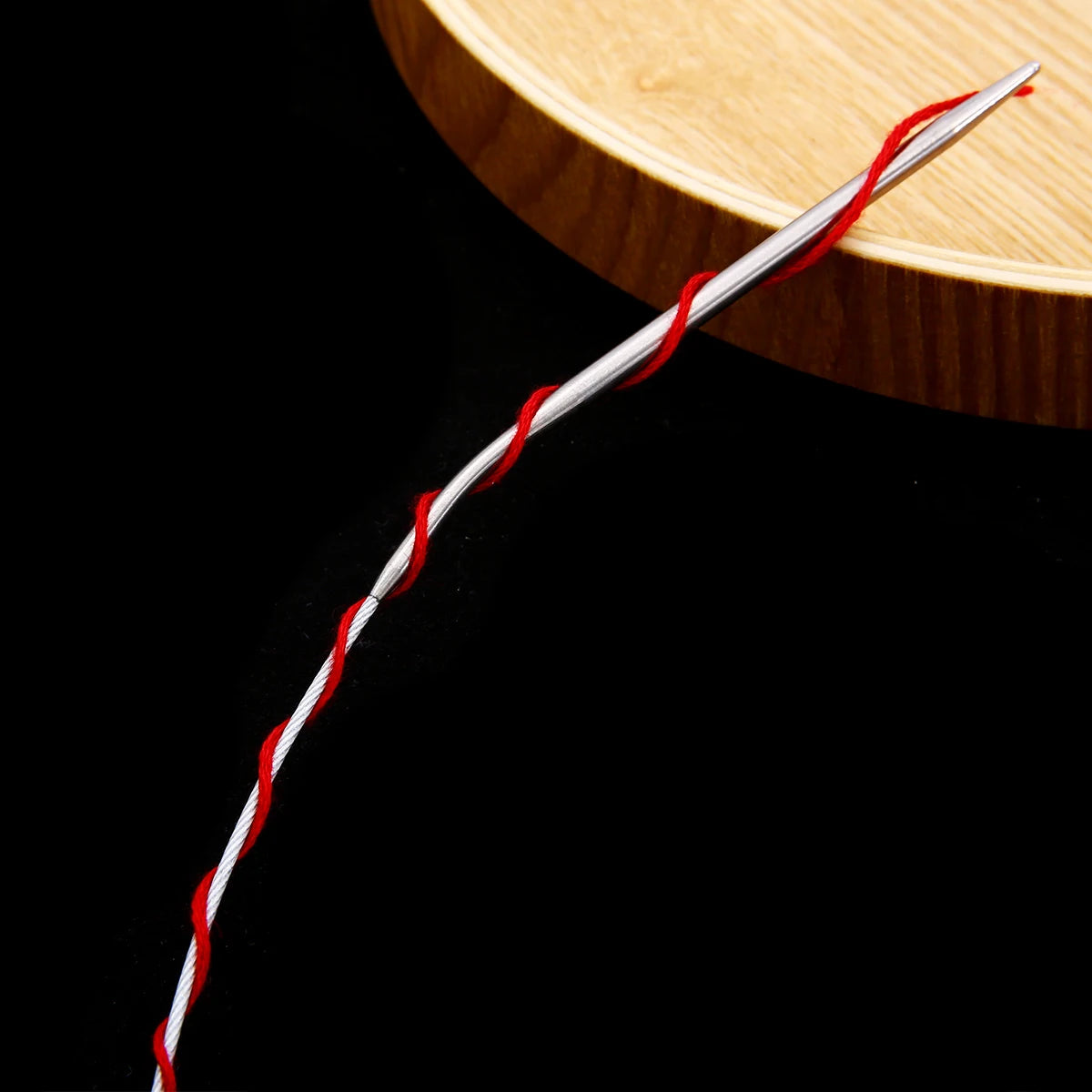 A single stainless steel circular knitting needle with red and white striped thread resting on a wooden surface.