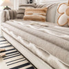 A beige plush velvet sofa protector cover with striped fabric and decorative pillows on a white sofa.