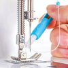 A hand is using a blue tool to thread a needle with a white thread on a metal tool.
