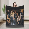 A photo of five women posing with a black fleece throw blanket in a studio setting.