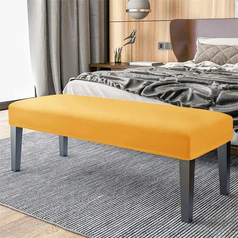 An orange velvet bench slipcover with secure straps placed on a gray striped rug in a bedroom setting.
