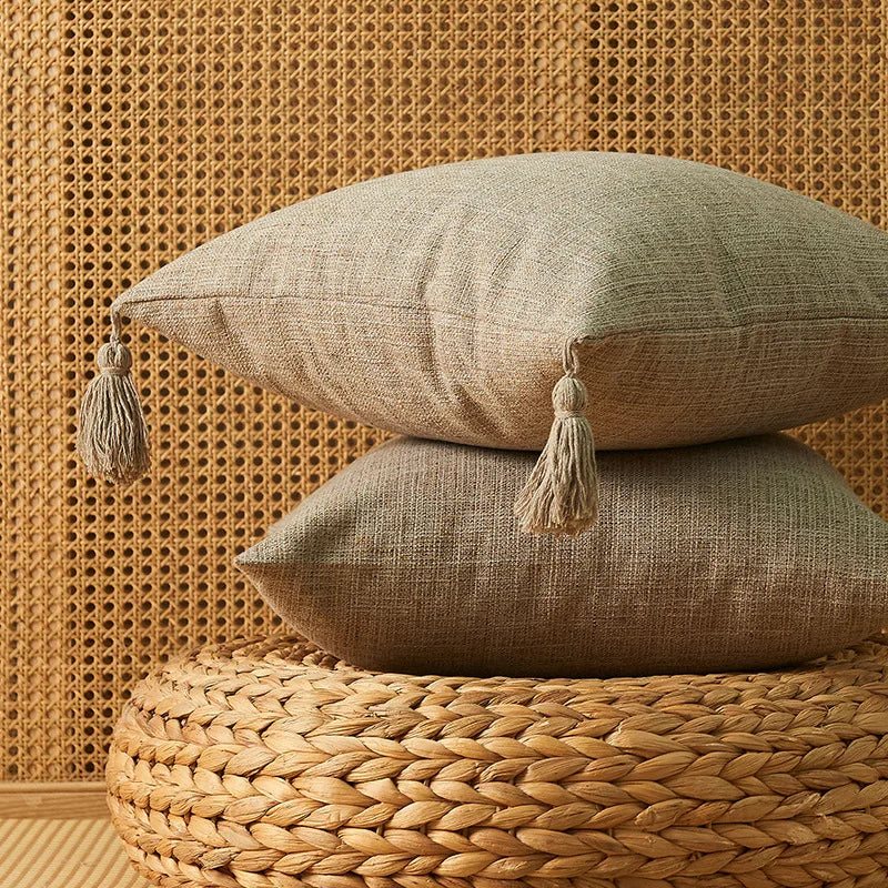 Two beige linen throw pillows resting on a woven natural fiber surface against a textured wall.