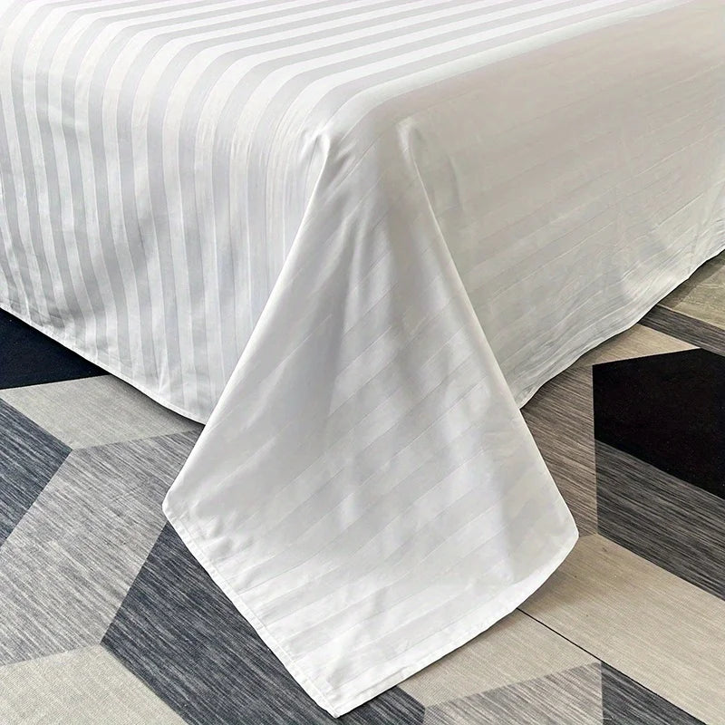 White luxury striped cotton flat sheet bedding draped on a gray and white tiled floor.