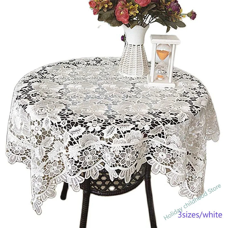 White floral lace tablecloth set with a vase of flowers and an hourglass on a dark table.