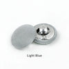A single light blue round fabric-covered shank button with a silver backing.