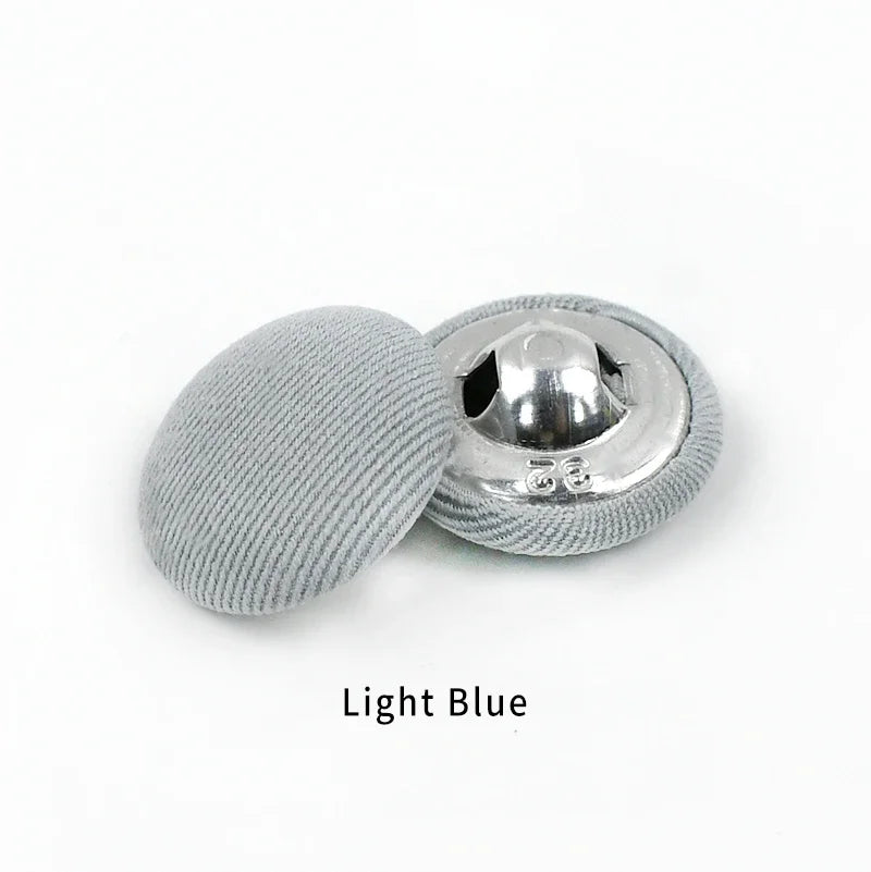 A single light blue round fabric-covered shank button with a silver backing.
