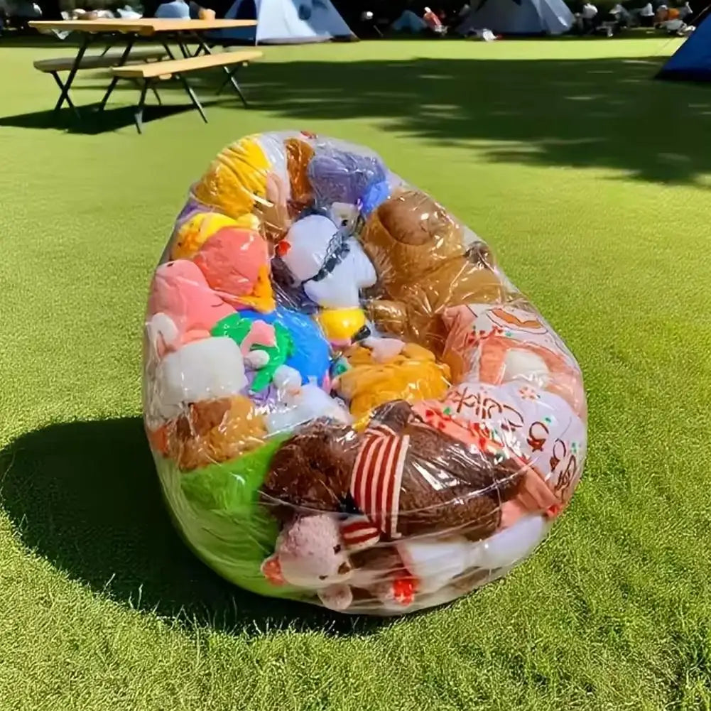 A large, transparent inflatable storage bag filled with various plush toys and stuffed animals on a green field.