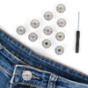 A pile of metal jeans buttons and a screwdriver are displayed on a piece of denim fabric.