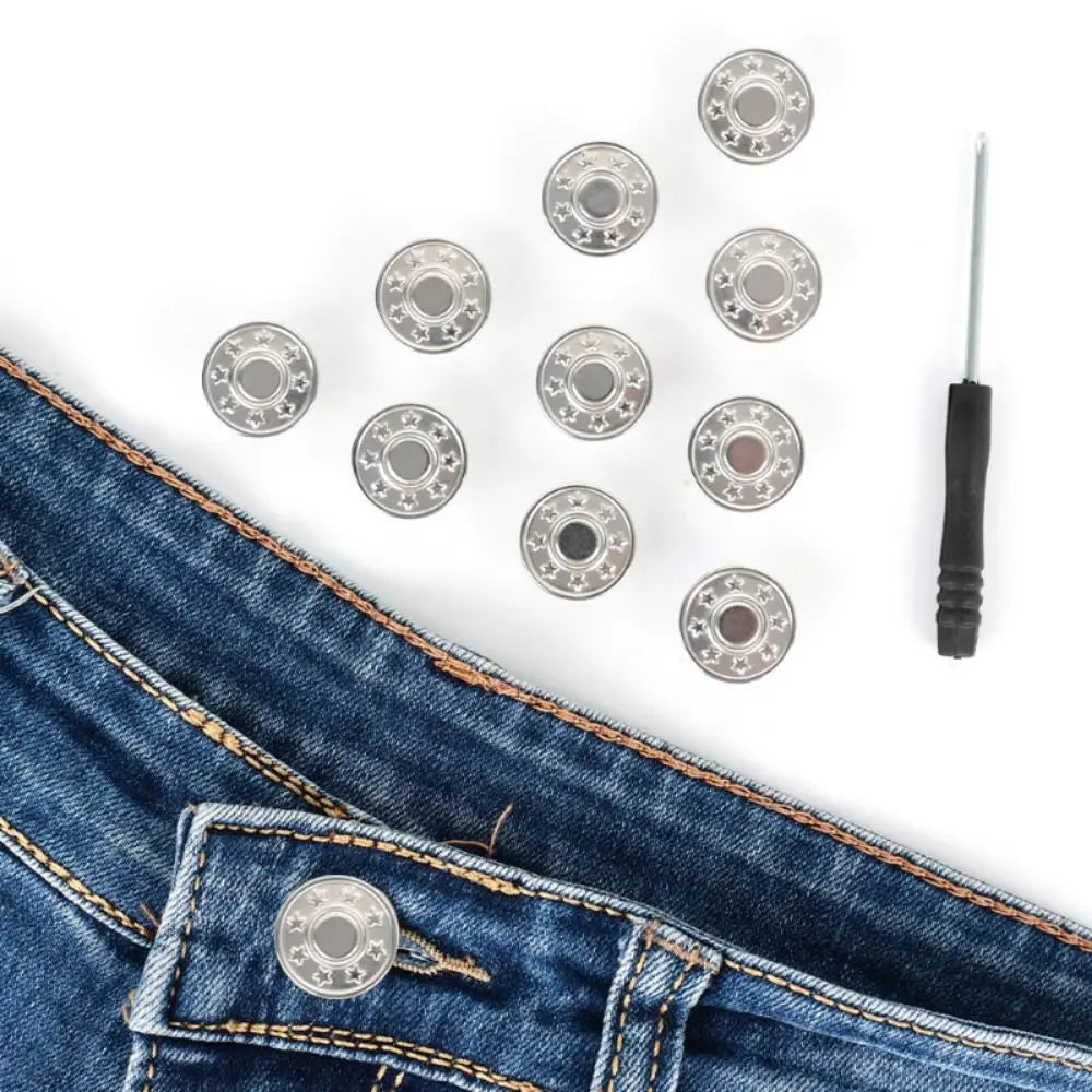 A pile of metal jeans buttons and a screwdriver are displayed on a piece of denim fabric.