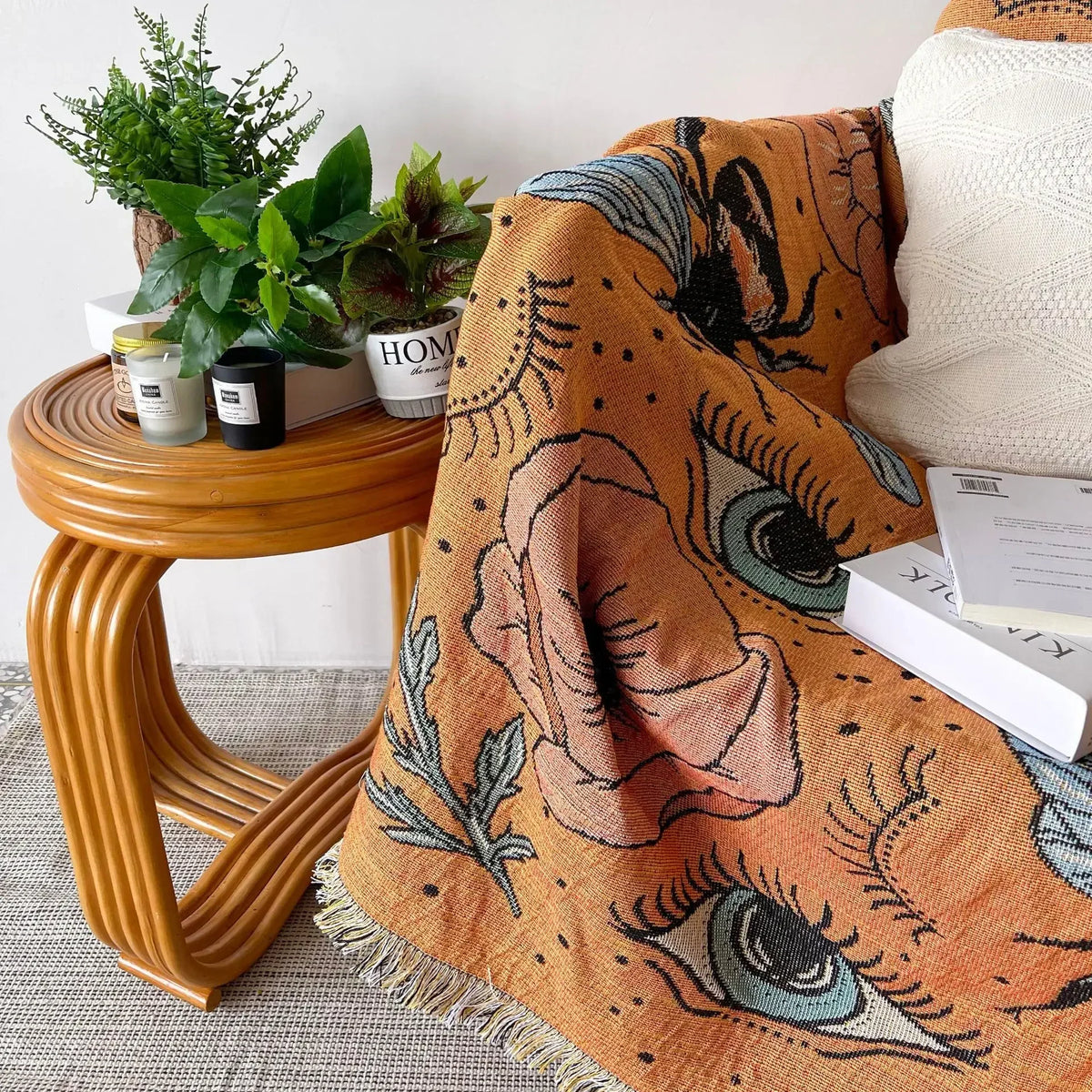 A bohemian geometric throw blanket in earthy tones draped next to potted greenery and a wooden stool.