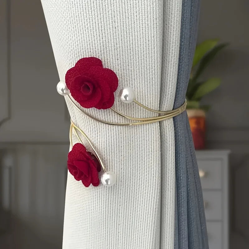 A close-up of a red rose pattern curtain tie featuring a fabric flower and adjustable metal buckles on a light gray curtain.