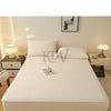 A white fitted bed sheet set with a quilted texture is displayed on a bed, next to warning labels.