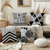 A collection of modern geometric print square pillowcases in black and gray patterns displayed on a sofa.