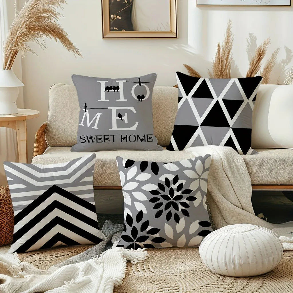 A collection of modern geometric print square pillowcases in black and gray patterns displayed on a sofa.