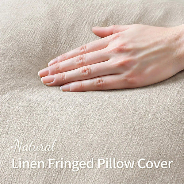 A hand gently rests on a natural linen fringed pillow cover.