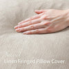 A hand gently touches a natural linen fringed pillow cover in a beige tone.