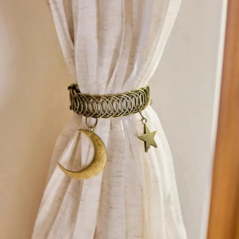 A close-up of a natural fiber curtain tieback featuring a woven rope clip with a gold star and a crescent moon charm.
