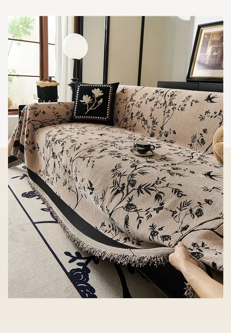A beige chenille sofa slipcover with a black floral pattern is draped on a light-colored rug.