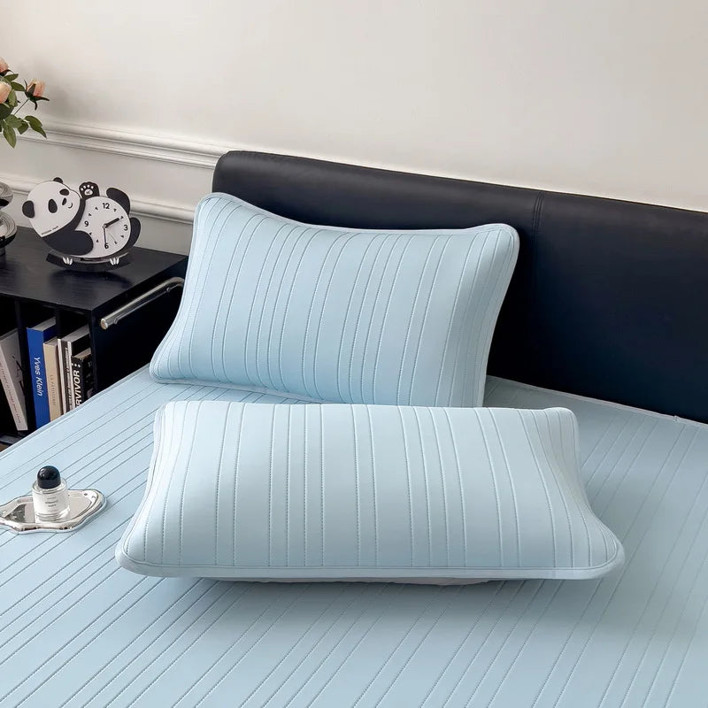 Light blue cooling ice silk bed pad placed on a bed, next to a dark headboard and books.