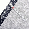 A precision metal sliding sewing gauge is shown diagonally across a gray fabric with a black and white floral pattern.