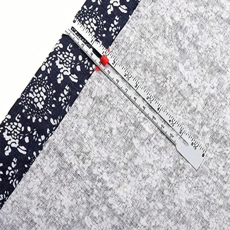 A precision metal sliding sewing gauge is shown diagonally across a gray fabric with a black and white floral pattern.