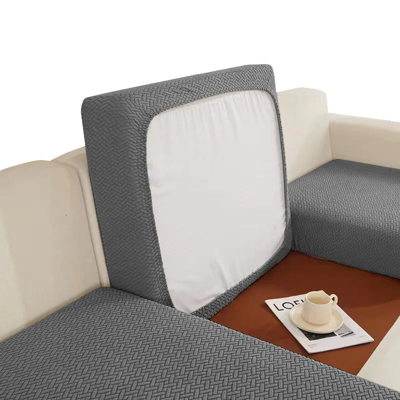 A gray woven cushion cover with a white insert is placed on a brown surface.