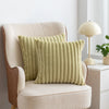 A light green faux fur stripe decorative throw pillow cover resting on a beige upholstered armchair.