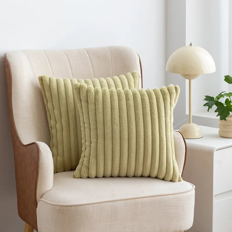 A light green faux fur stripe decorative throw pillow cover resting on a beige upholstered armchair.