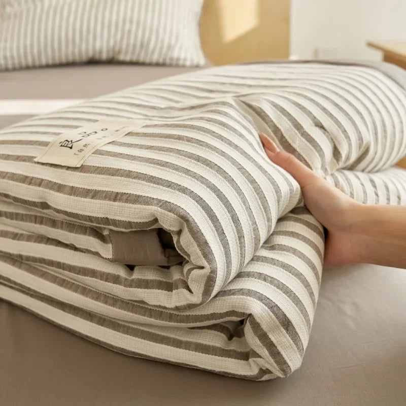 A striped white and gray luxury jacquard summer quilt folded on a bed.