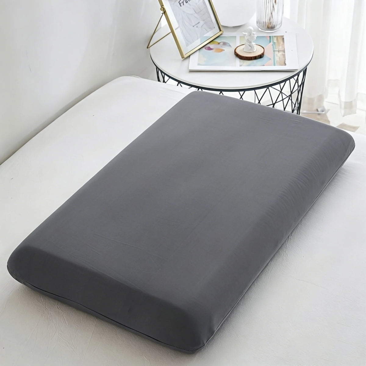 A gray ice silk cooling pillowcase lying on a white surface next to a small table with decorative items.