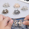 A collection of adjustable metal waist clips in silver and gold tones displayed on a denim fabric.