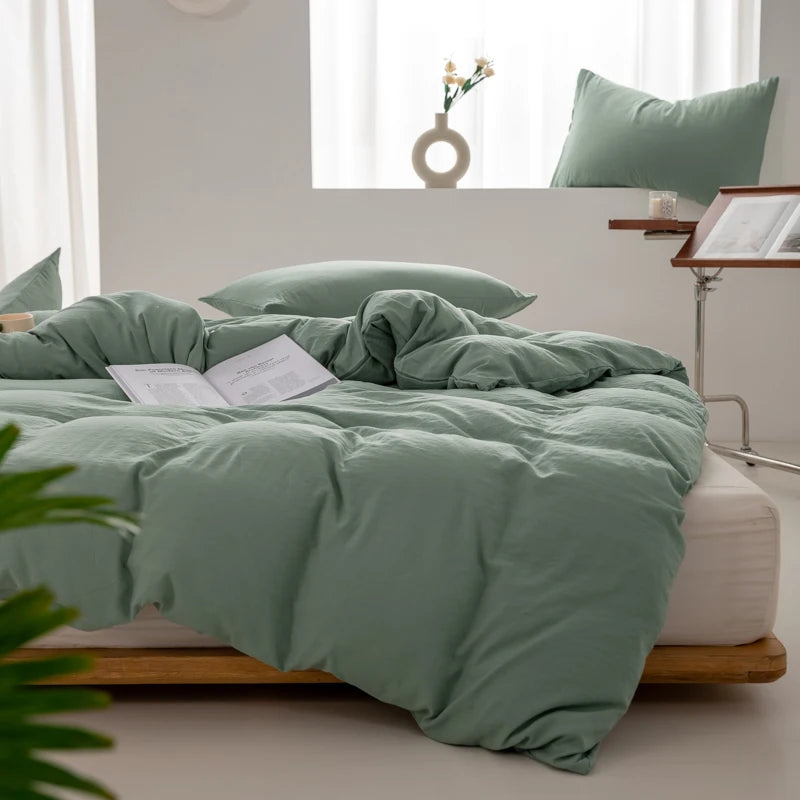 A light sage green minimalist duvet cover spread on a bed with white linens and natural wood frame.