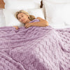 A woman rests her head on a white pillow while wrapped in a purple checkered fleece throw blanket.